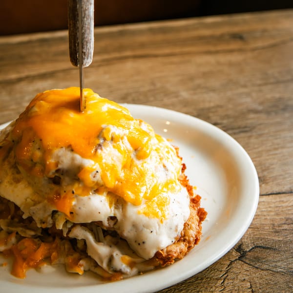 Hearty breakfast dish with hash browns, sausage gravy, melted cheddar cheese, and a knife.