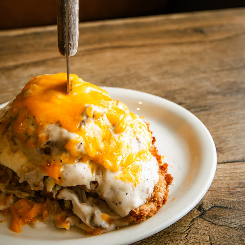 Hearty breakfast dish with hash browns, sausage gravy, melted cheddar cheese, and a knife.