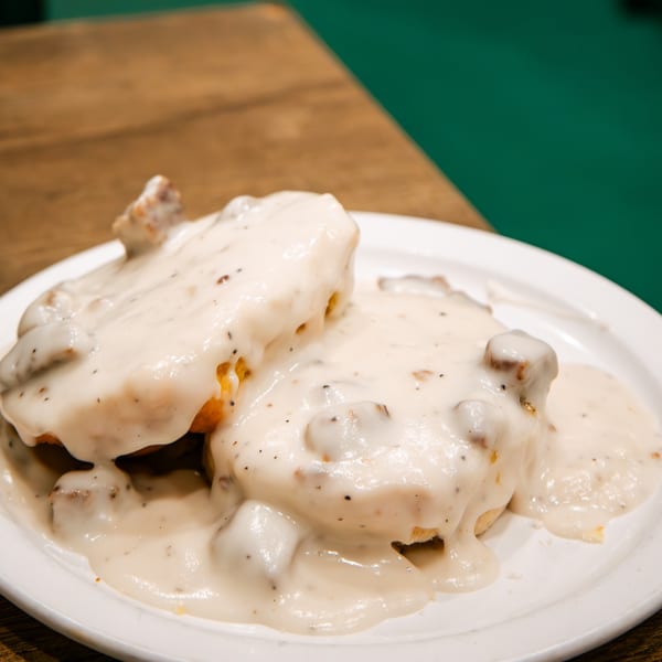 Biscuits and gravy on a white plate, with a wooden table and green wall in the background.