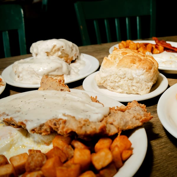 Plates of biscuits and gravy, fried chicken, and home fries on a wooden table.