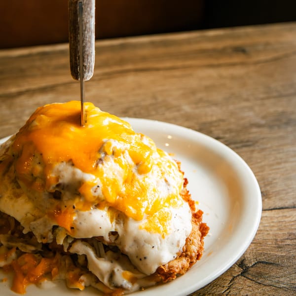 A knife piercing a stack of hash browns, gravy, and melted cheese on a white plate.