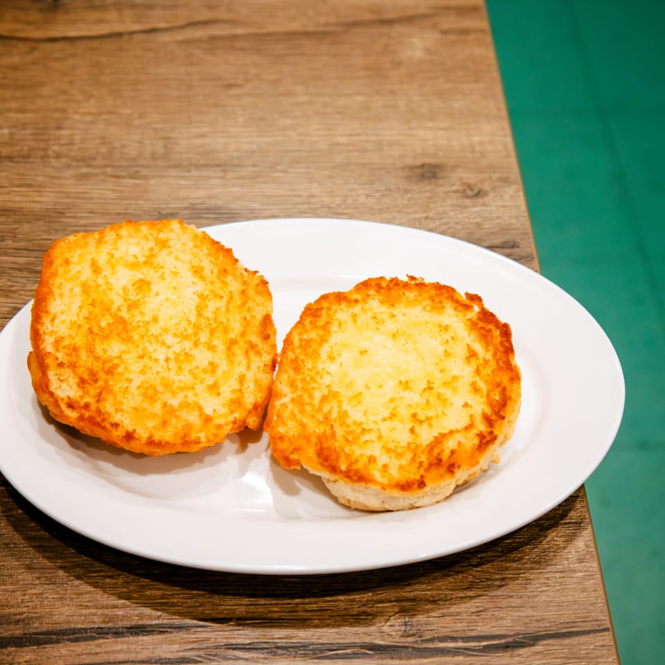 Two golden-brown toasted garlic bread slices on a white plate, on a wooden table.
