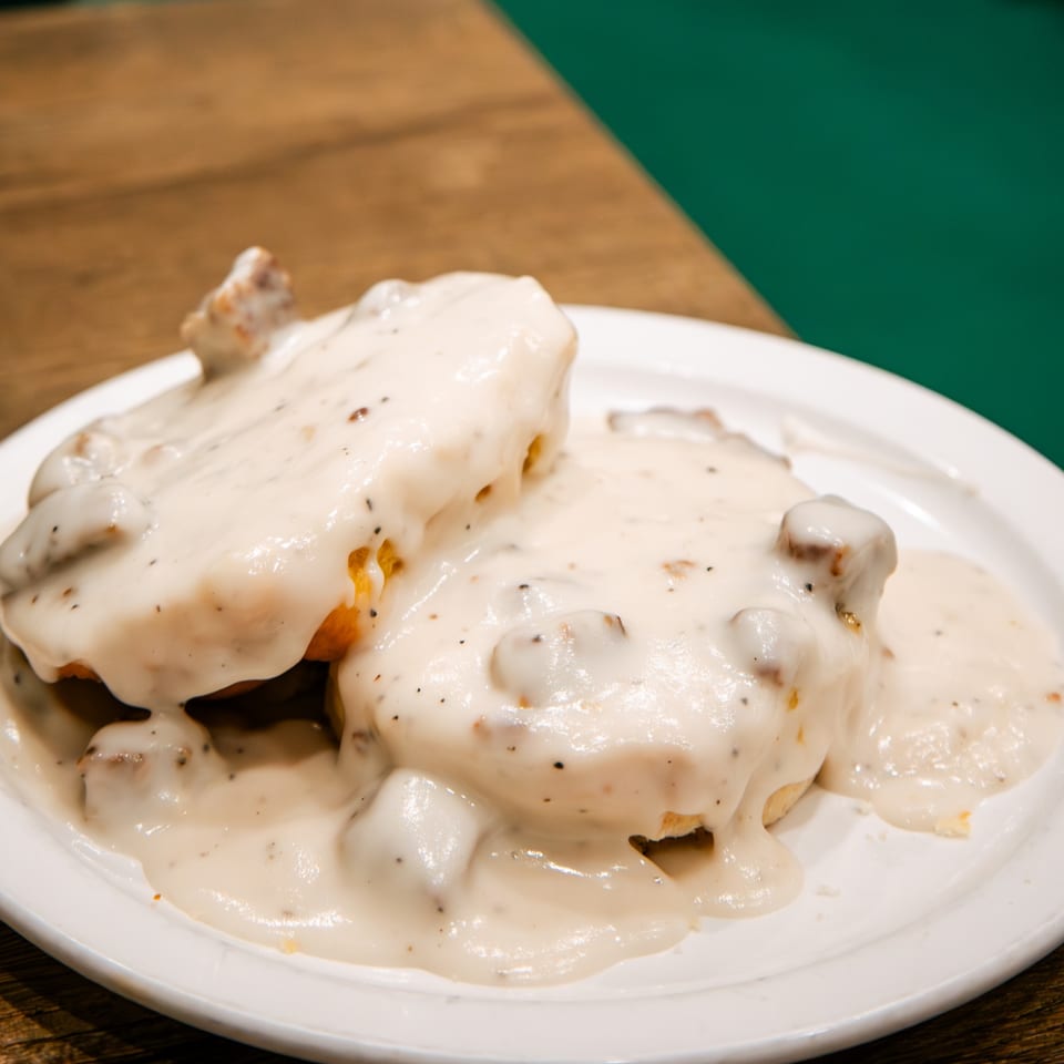 Two biscuits covered in creamy sausage gravy with black pepper on a white plate.