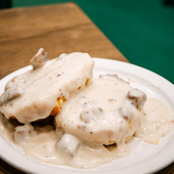 Biscuits and gravy on a white plate, with a wooden table and green background.