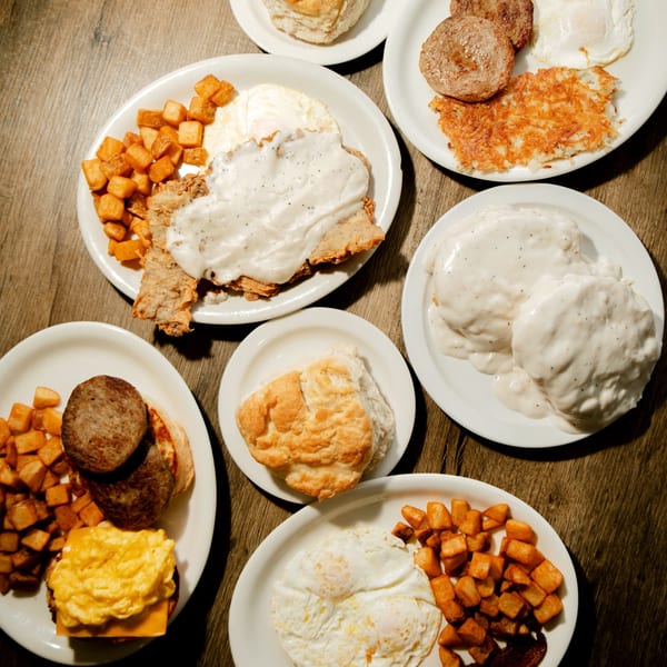Overhead view of multiple plates of breakfast food, including biscuits, gravy, eggs, sausage, and potatoes.