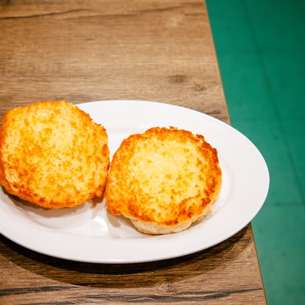 Two golden-brown toasted buns on a white plate, on a wooden table.