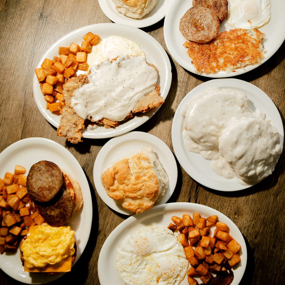 Overhead view of multiple plates of classic American breakfast foods on a wooden table.