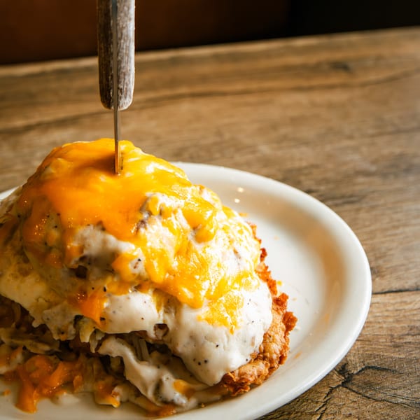 A knife stuck into a stack of hash browns, gravy, and melted cheese on a white plate.