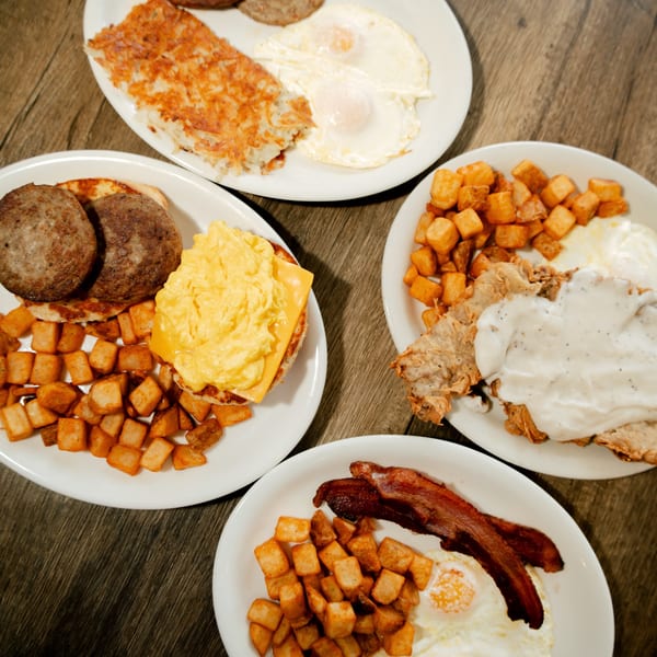 Four plates of breakfast food, including hash browns, eggs, sausage, bacon, and country fried steak.