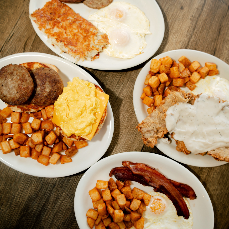 Four plates of breakfast food, including hash browns, eggs, sausage, bacon, and country fried steak.