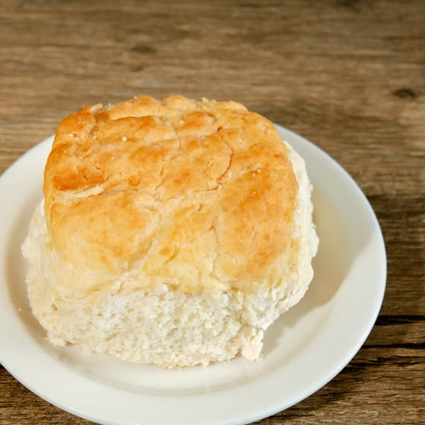 Golden-brown biscuit on a white plate, resting on a rustic wooden table.
