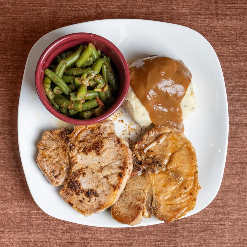 Two grilled pork chops with mashed potatoes and gravy, and a side of green beans.
