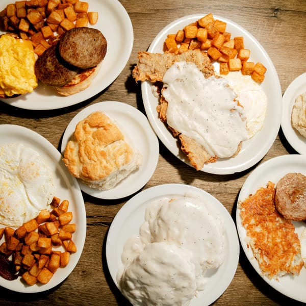 Multiple plates of classic American breakfast foods, including biscuits, gravy, eggs, sausage, and hash browns.